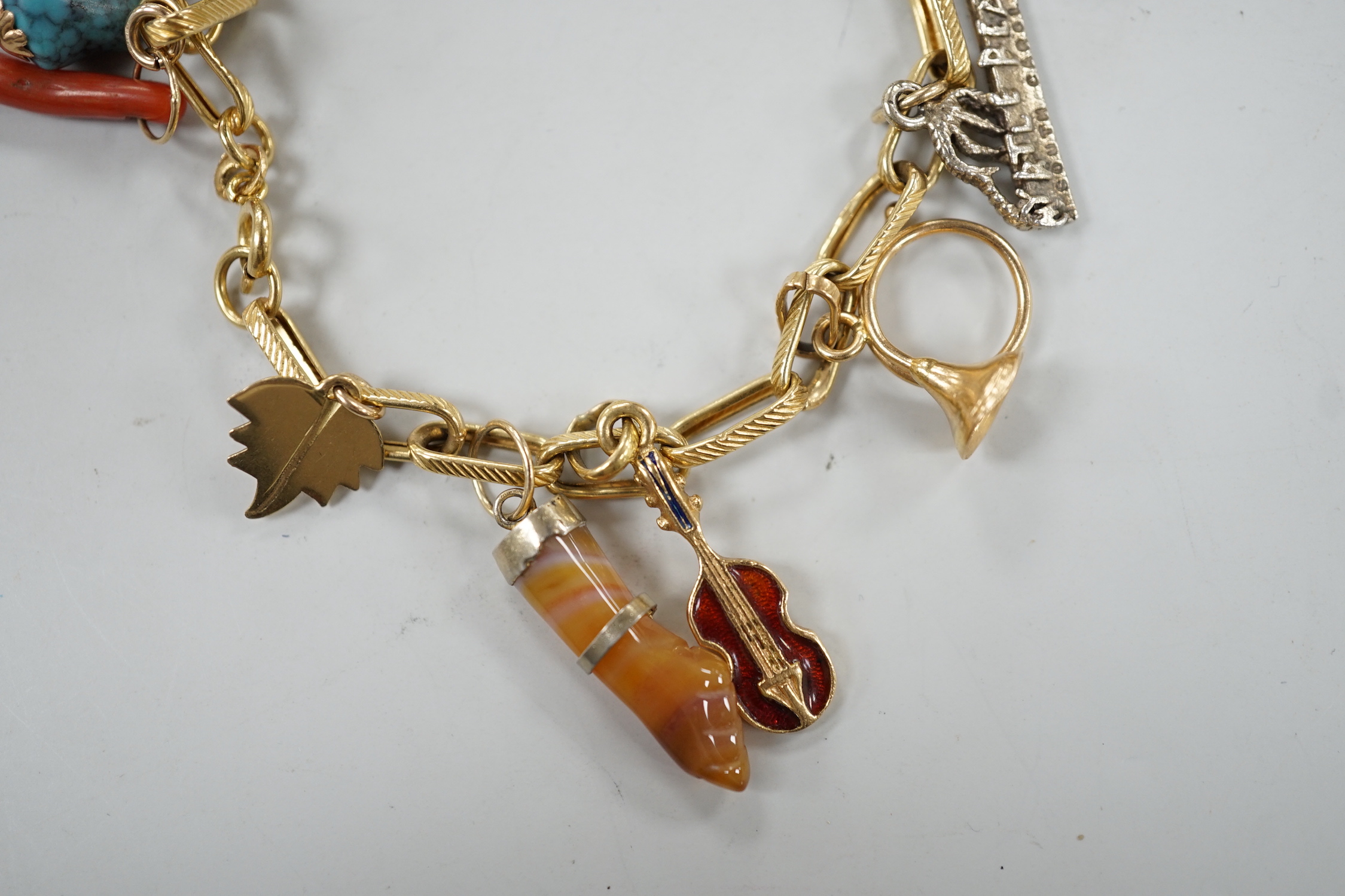 A modern Italian yellow metal charm bracelet, hung with eleven assorted charms, including 750 and enamel jockey cap, agate clasped hand and 750 acorn